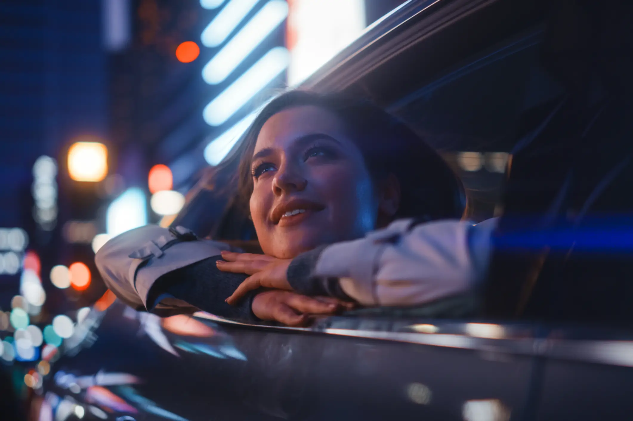 Woman enjoying city lights from car window.