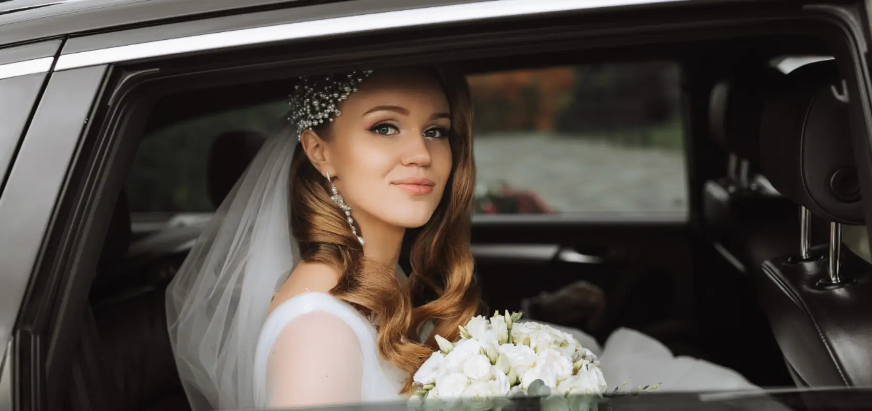 Bride in car holding bouquet, smiling softly.