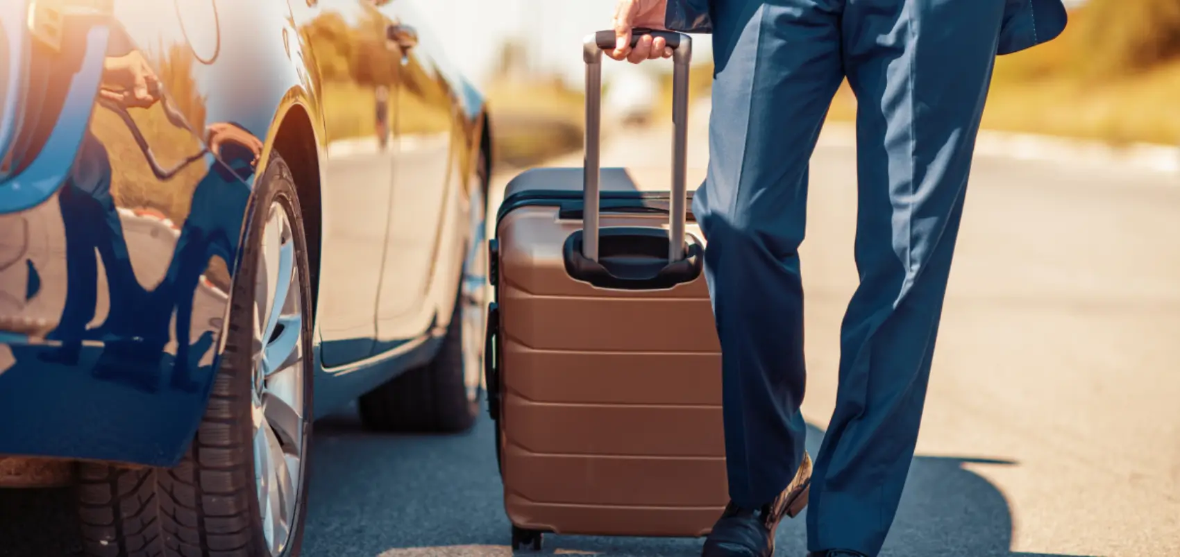 Person with suitcase beside parked car.
